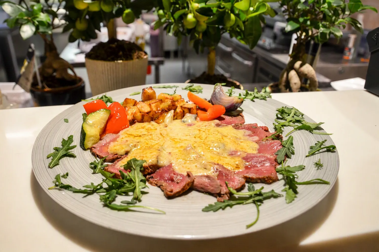 Tynne skiver oksekjøtt under gratinert ost, med ruccola og grillede grønnsaker