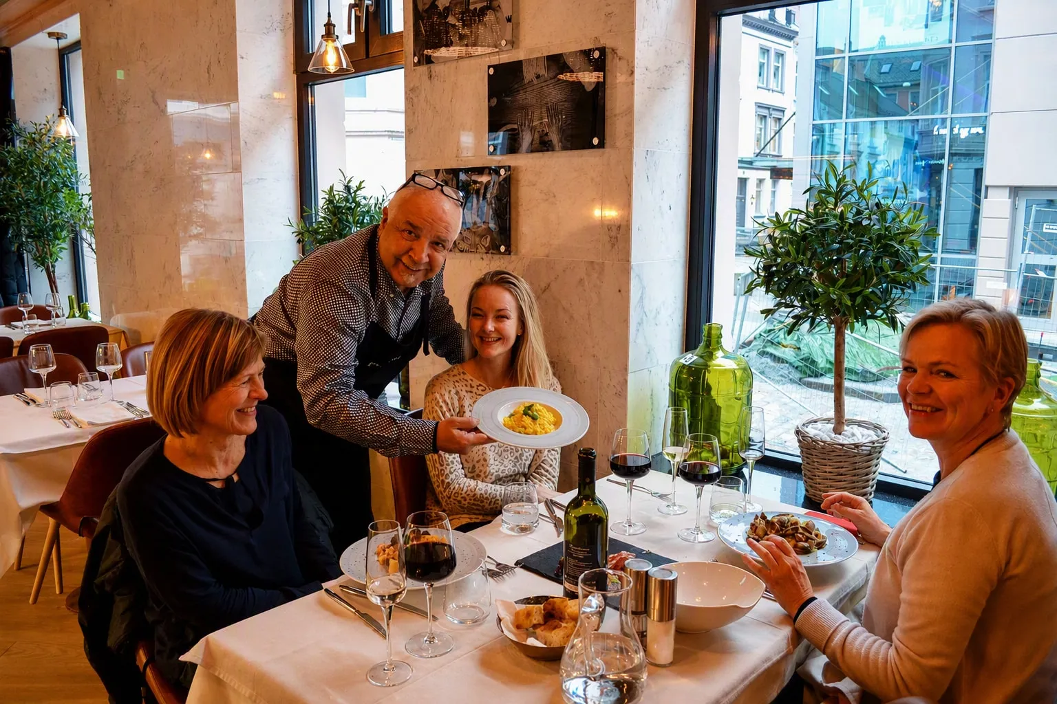 Verten setter fram en pastarett til gjester ved et vindusbord